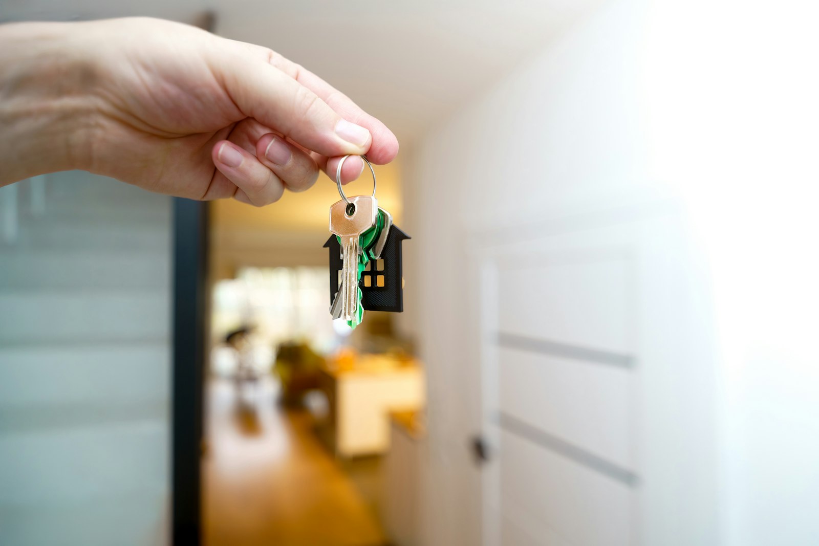 A hand holding a set of house keys on a house-shaped fob in a doorway