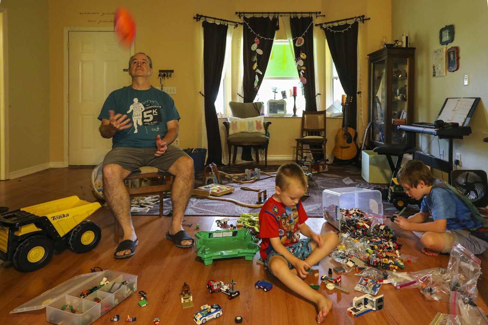A parent sitting with two young children among toys in a living room
