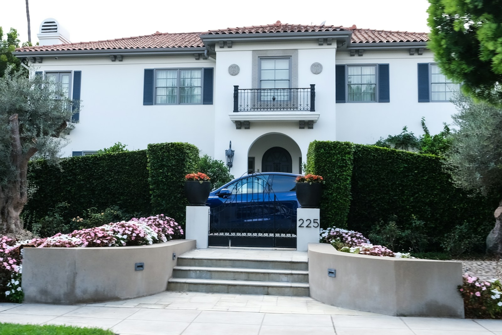 A blue car behind wrought iron gates in front of a large white house
