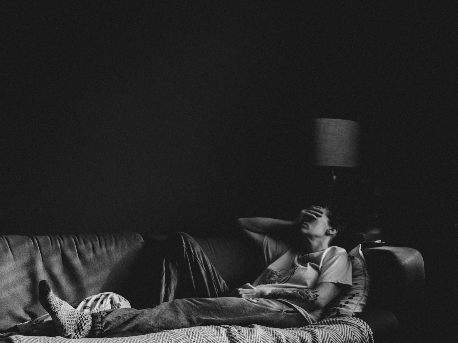 A person lying on a sofa in a dark room with a hand over their face