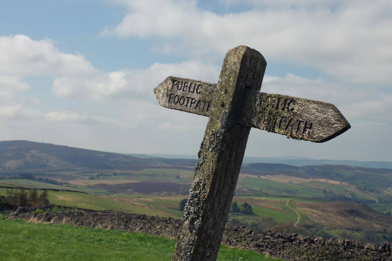 A weathered wooden public footpath signpost above open countryside